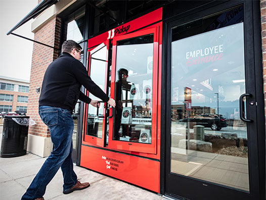 A man opens the door to a red-framed employee entrance of a sandwich franchise building.