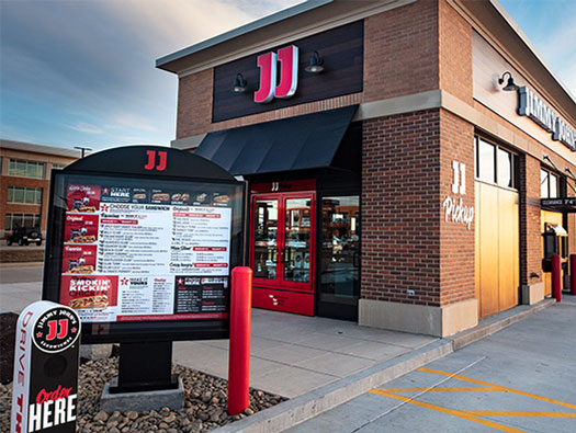 Exterior view of a Jimmy John's sandwich franchise with a drive-thru menu board in the foreground.